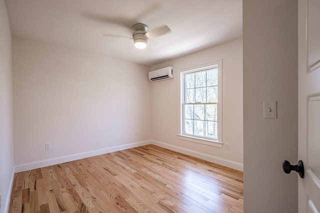 spare room with an AC wall unit, light wood-style floors, ceiling fan, and baseboards