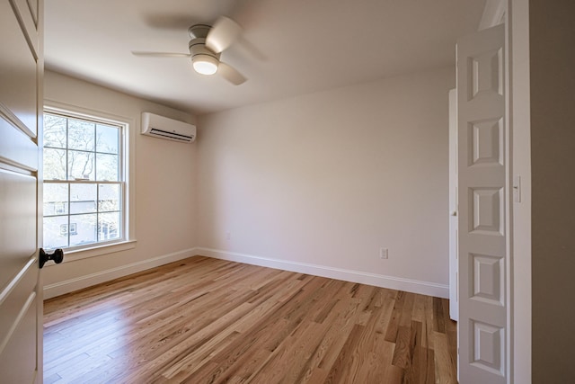 empty room featuring a ceiling fan, baseboards, a wall unit AC, and light wood-type flooring