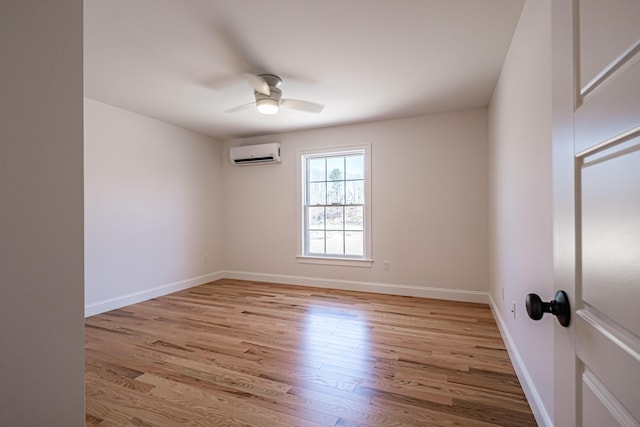 empty room featuring light wood-type flooring, a ceiling fan, baseboards, and a wall unit AC