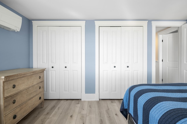 bedroom featuring light hardwood / wood-style floors, multiple closets, and a wall mounted air conditioner