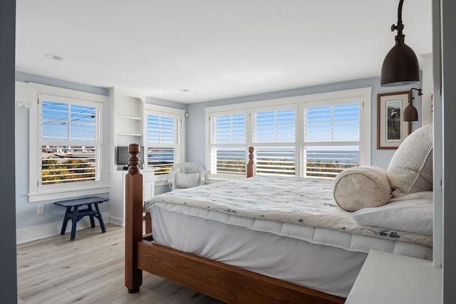 bedroom with a water view, multiple windows, and light hardwood / wood-style floors