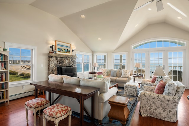 living room with a baseboard radiator, a stone fireplace, dark hardwood / wood-style flooring, ceiling fan, and vaulted ceiling