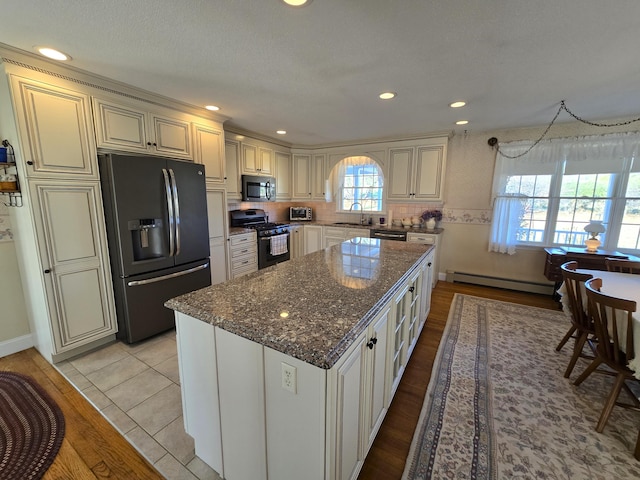 kitchen featuring a center island, stainless steel appliances, dark stone countertops, baseboard heating, and light hardwood / wood-style flooring