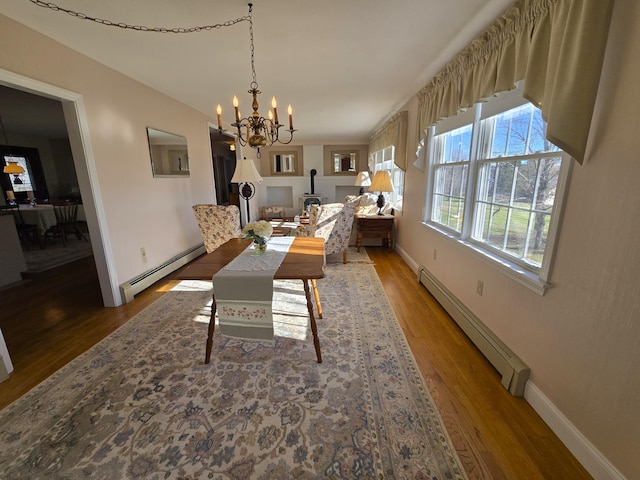 dining area featuring baseboard heating, a notable chandelier, a wood stove, and wood-type flooring