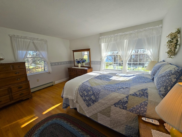 bedroom featuring wood-type flooring, multiple windows, and a baseboard heating unit