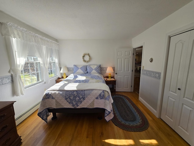 bedroom featuring a baseboard heating unit, hardwood / wood-style floors, a textured ceiling, and a closet