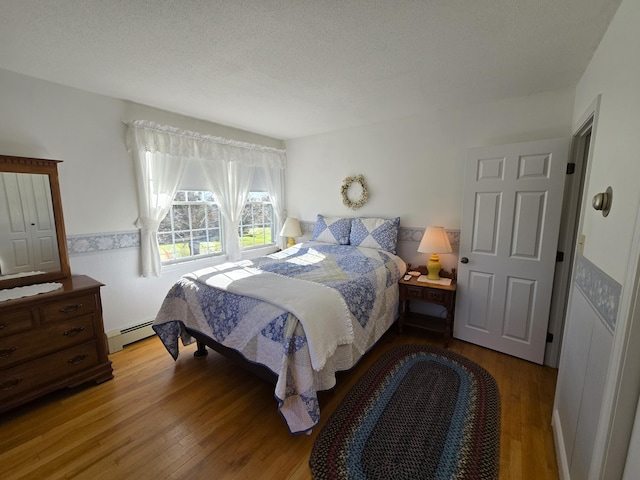 bedroom with hardwood / wood-style floors, a baseboard radiator, and a textured ceiling