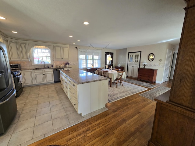 kitchen with stainless steel appliances, light stone counters, a center island, light hardwood / wood-style flooring, and decorative light fixtures