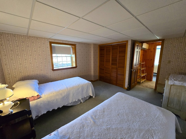 bedroom with a wall mounted AC, carpet floors, and a drop ceiling