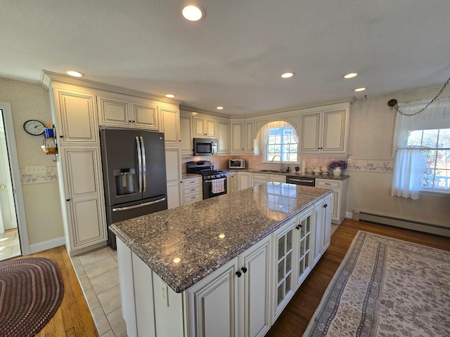 kitchen featuring light wood-type flooring, appliances with stainless steel finishes, a baseboard heating unit, and plenty of natural light