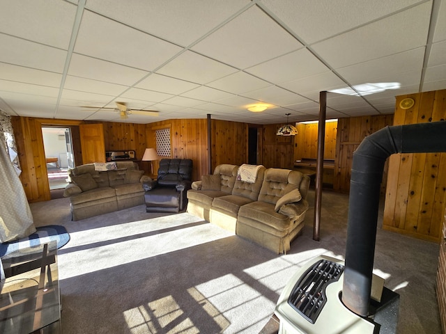 living room with carpet, a paneled ceiling, wood walls, and ceiling fan