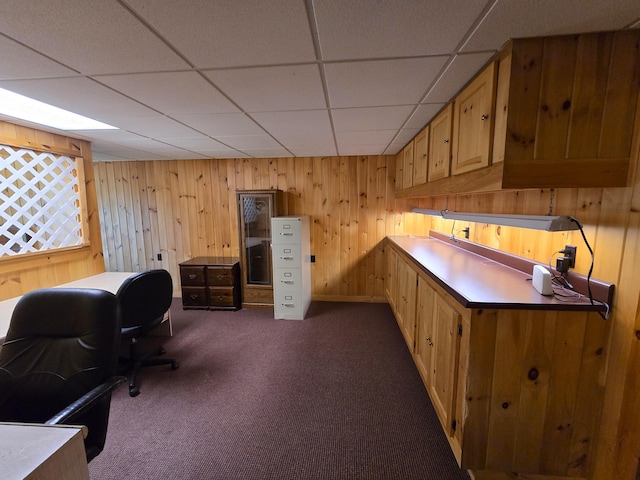 office area with a drop ceiling, wooden walls, and dark carpet