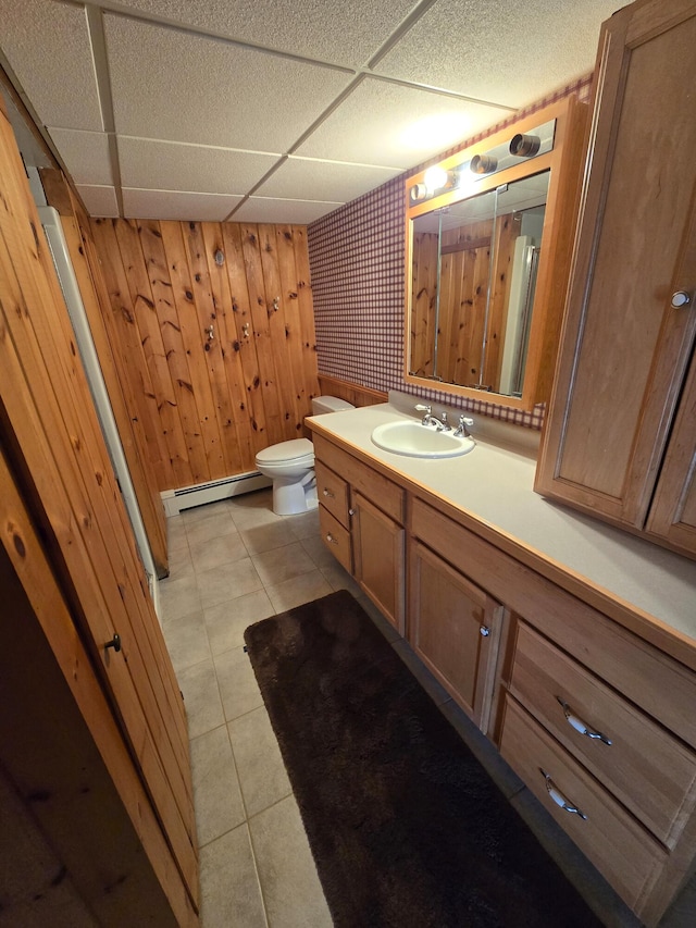 bathroom with a paneled ceiling, vanity, wooden walls, a baseboard heating unit, and toilet