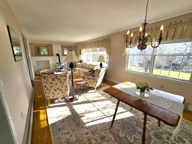 dining room featuring wood-type flooring, a baseboard radiator, a wood stove, and a notable chandelier