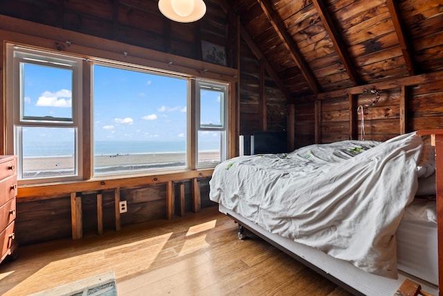 bedroom featuring vaulted ceiling with beams, light hardwood / wood-style flooring, multiple windows, and a water view