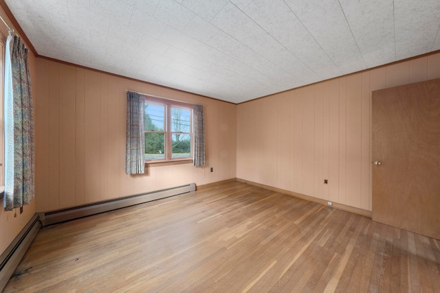 empty room with a baseboard heating unit, light hardwood / wood-style floors, and wood walls