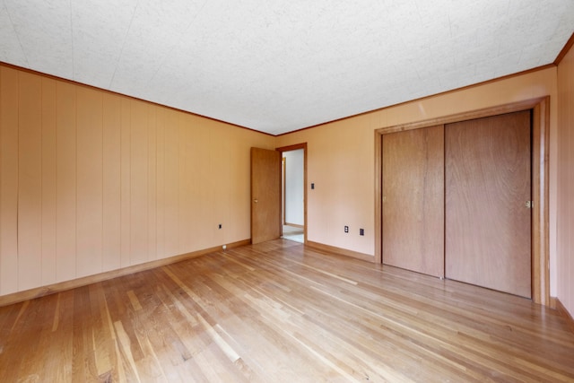 unfurnished bedroom with ornamental molding, light wood-type flooring, wood walls, and a closet