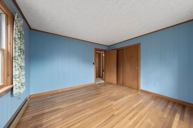 unfurnished room featuring light hardwood / wood-style floors, a baseboard radiator, wooden walls, and crown molding