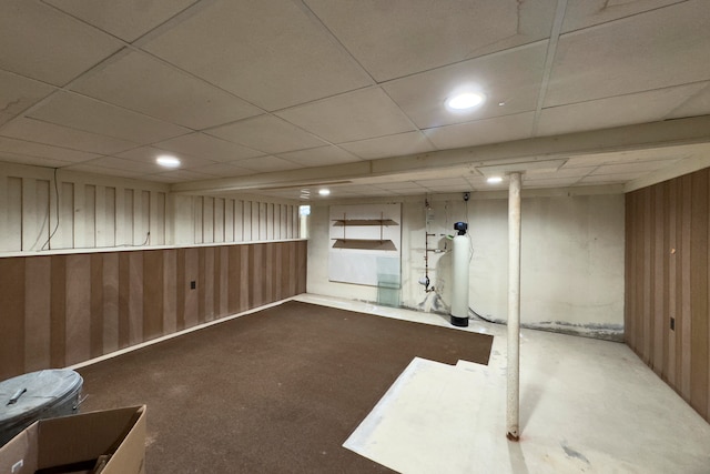 basement featuring wood walls, a drop ceiling, and dark carpet