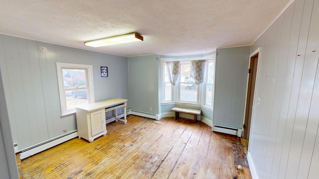 interior space with baseboard heating, light hardwood / wood-style flooring, a textured ceiling, and wood walls