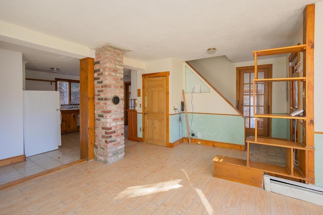 empty room with decorative columns, light hardwood / wood-style floors, and a baseboard radiator