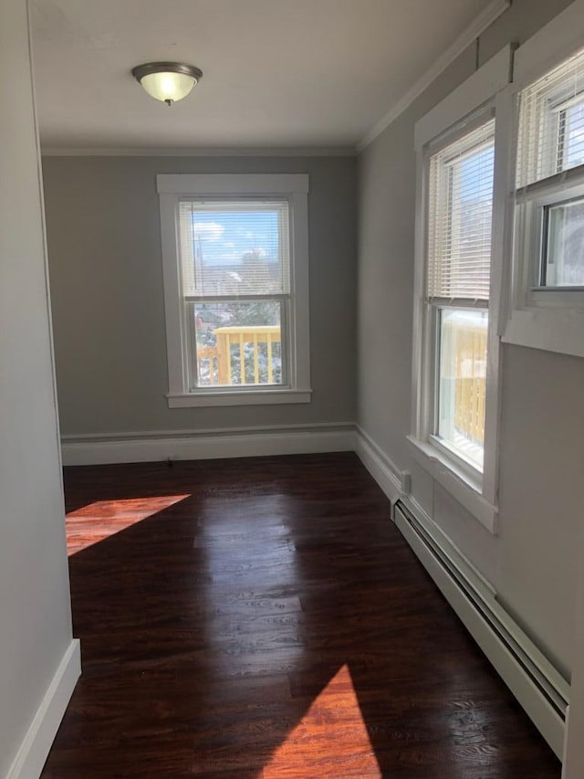 spare room featuring dark wood-type flooring, a healthy amount of sunlight, ornamental molding, and baseboard heating