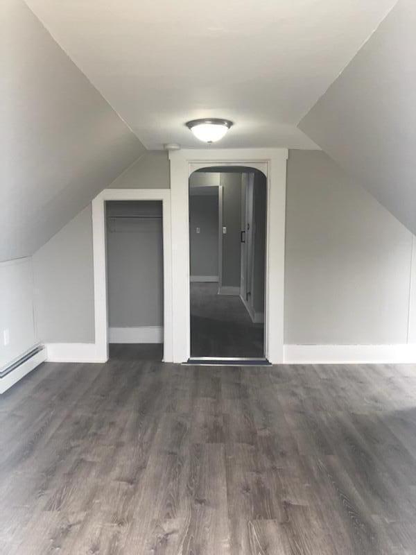 additional living space featuring a baseboard heating unit, dark wood-type flooring, and vaulted ceiling