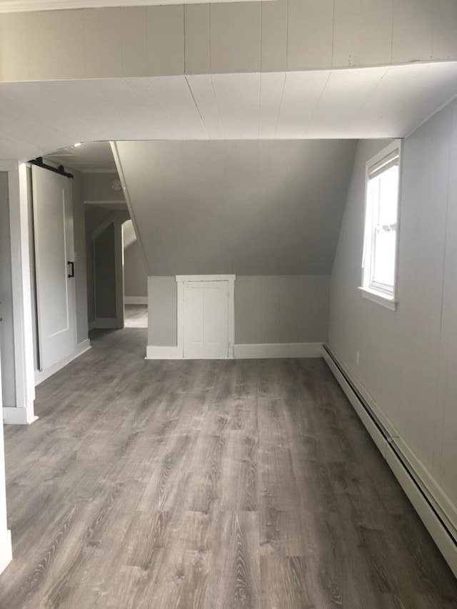 additional living space with vaulted ceiling, a baseboard radiator, a barn door, and hardwood / wood-style floors