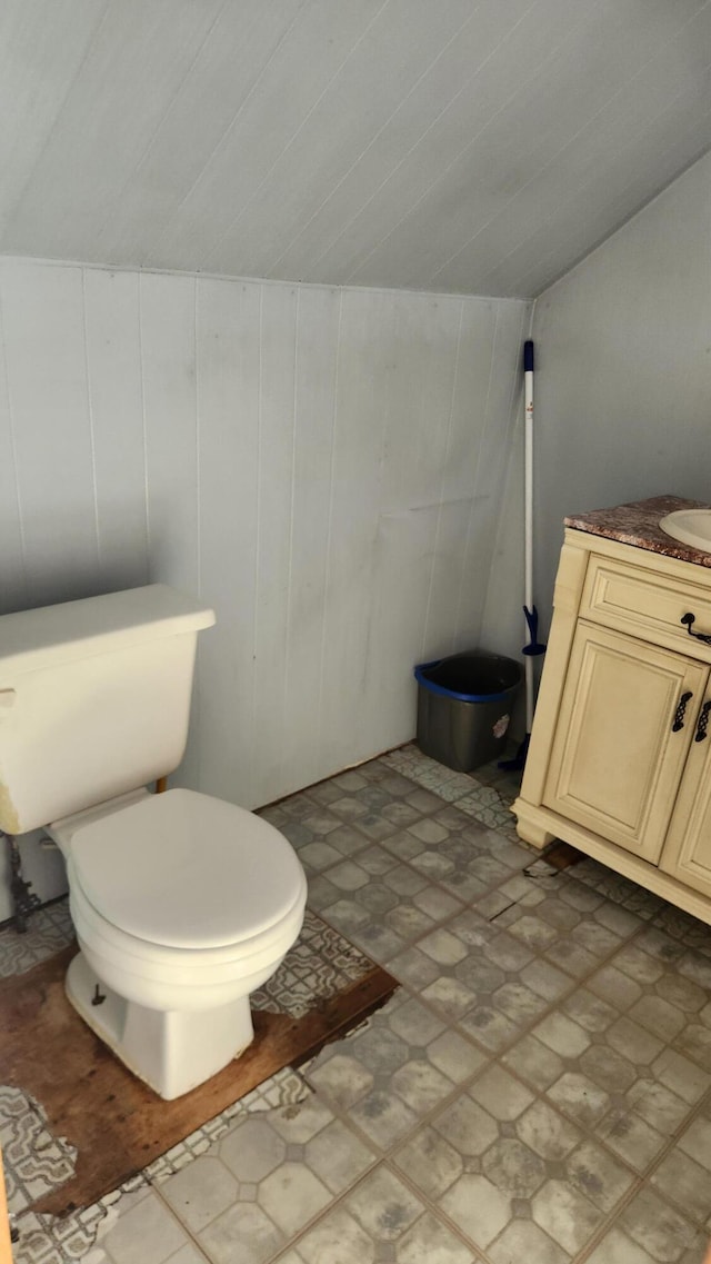 bathroom featuring vanity, lofted ceiling, toilet, and wooden walls