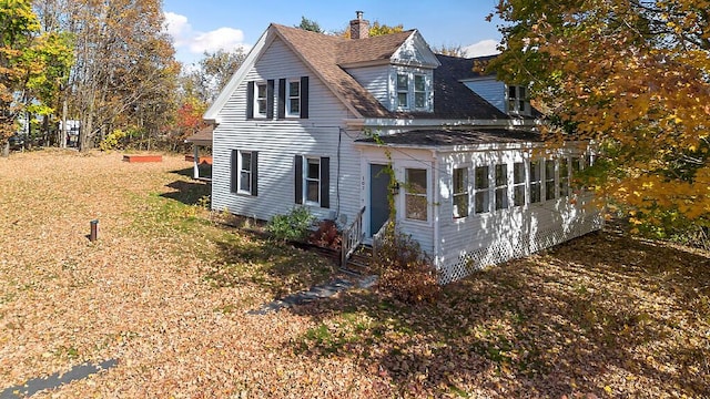 view of front of house with a chimney, a sunroom, and a shingled roof