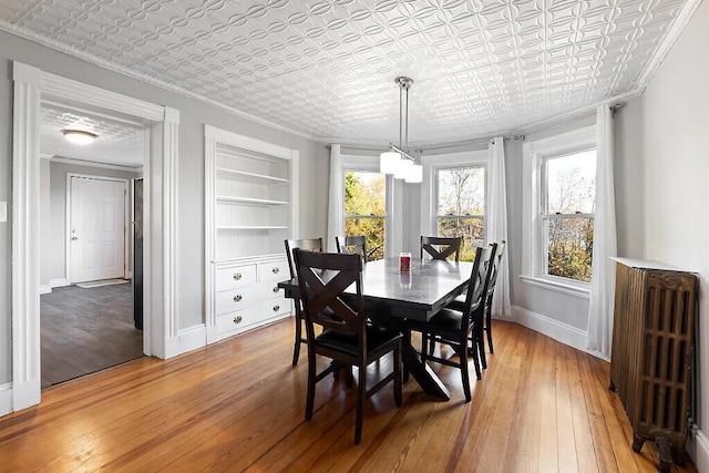 dining area with ornamental molding, light wood-style flooring, an ornate ceiling, and radiator heating unit