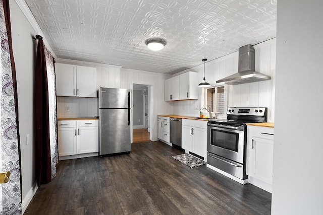 kitchen with wall chimney range hood, butcher block counters, stainless steel appliances, decorative light fixtures, and white cabinets