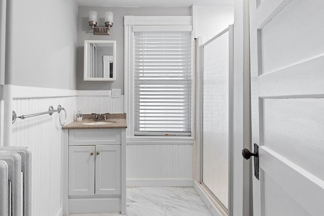 bathroom featuring a shower with shower door, wainscoting, marble finish floor, vanity, and radiator heating unit