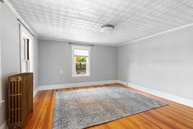empty room featuring ornamental molding, wood finished floors, an ornate ceiling, and radiator heating unit