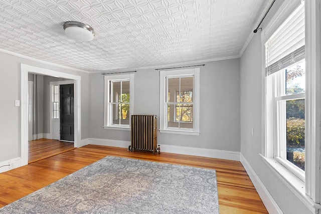empty room featuring an ornate ceiling, wood finished floors, radiator heating unit, ornamental molding, and baseboards