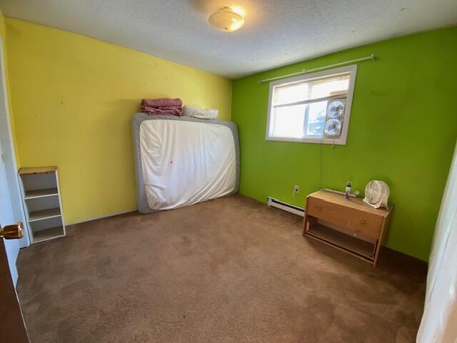 unfurnished bedroom with baseboard heating, dark carpet, and a textured ceiling