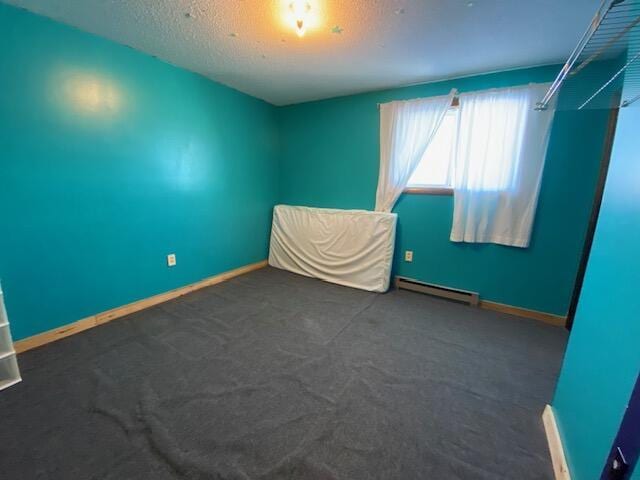 empty room with a baseboard heating unit, a textured ceiling, and dark carpet