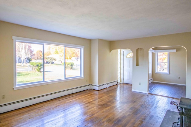 32 Morison Ave, Wells, ME 04090 - unfurnished living room featuring arched walkways, baseboard heating, wood finished floors, and baseboards