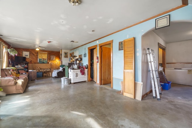 interior space with ornamental molding, concrete floors, ceiling fan, and wooden walls