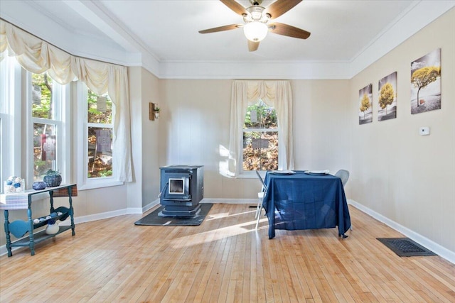 sitting room featuring a wood stove, hardwood / wood-style flooring, ceiling fan, and crown molding