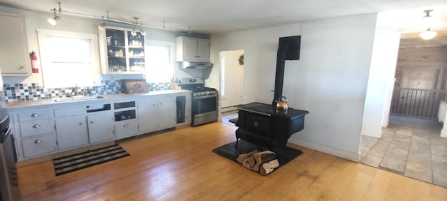 1334 Carmel Rd N, Hampden, ME 04444 - kitchen featuring gas stove, a sink, a wood stove, under cabinet range hood, and backsplash