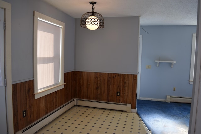 unfurnished dining area featuring wood walls, a textured ceiling, and baseboard heating