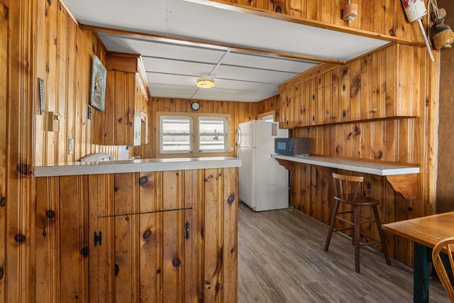 kitchen featuring hardwood / wood-style flooring, a breakfast bar area, kitchen peninsula, white refrigerator, and wood walls