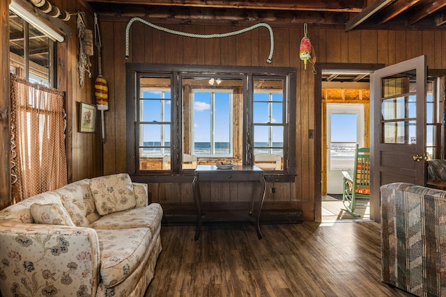 living area with a water view, beamed ceiling, wooden walls, and dark hardwood / wood-style floors