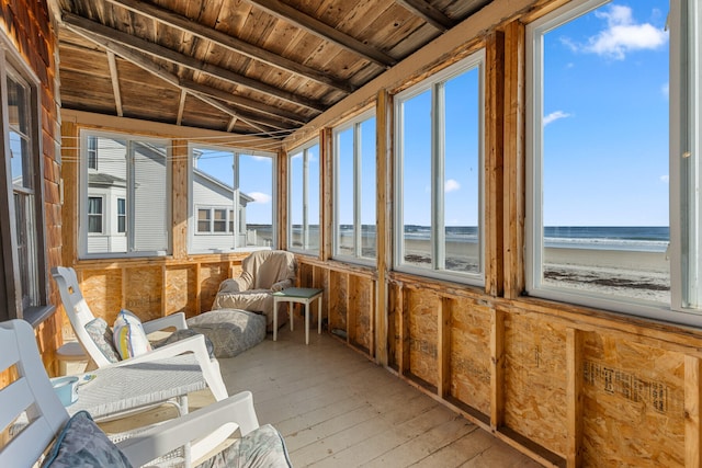 unfurnished sunroom with wooden ceiling, a water view, a beach view, and plenty of natural light