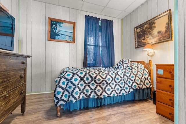 bedroom with a paneled ceiling, hardwood / wood-style flooring, and wood walls