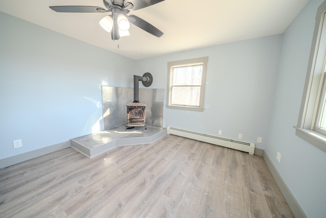 unfurnished living room with light hardwood / wood-style flooring, a wood stove, a baseboard radiator, and ceiling fan