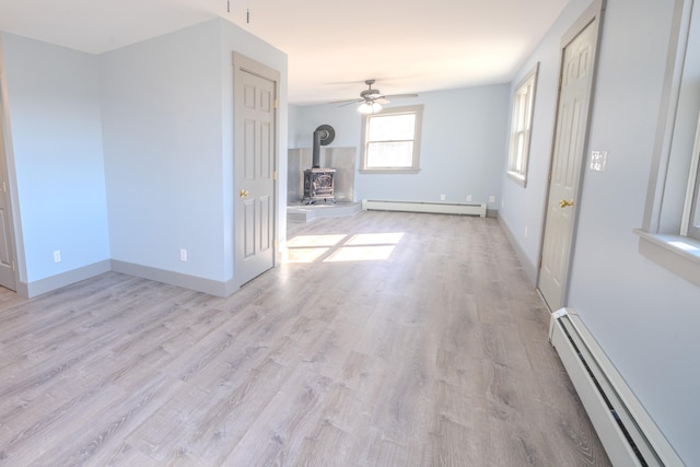 unfurnished living room with a baseboard heating unit, light hardwood / wood-style flooring, a wood stove, and ceiling fan