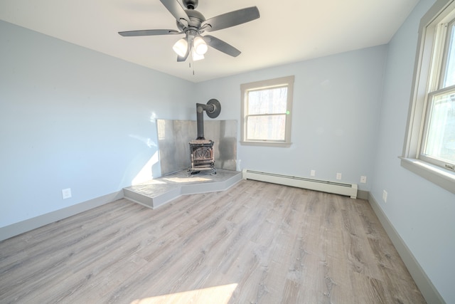 unfurnished living room featuring light hardwood / wood-style floors, a wood stove, baseboard heating, and ceiling fan