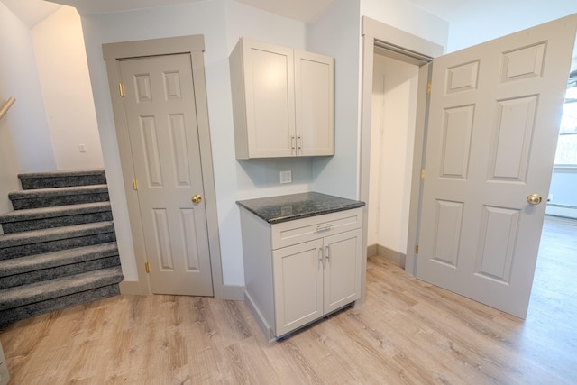 kitchen with white cabinetry, light wood-type flooring, and dark stone counters